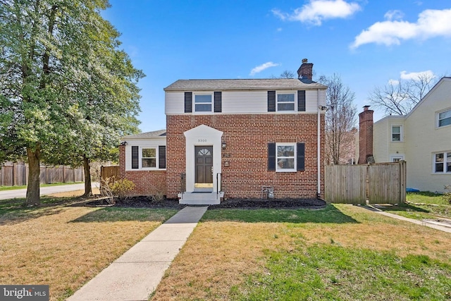 traditional-style house with brick siding, a chimney, a front yard, and fence