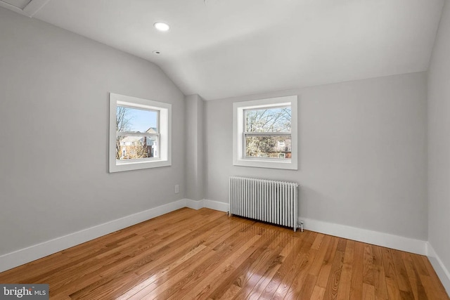 unfurnished room featuring light wood-style flooring, a healthy amount of sunlight, radiator heating unit, and lofted ceiling