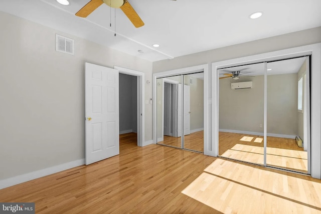 unfurnished bedroom featuring light wood finished floors, visible vents, multiple closets, recessed lighting, and a wall mounted AC