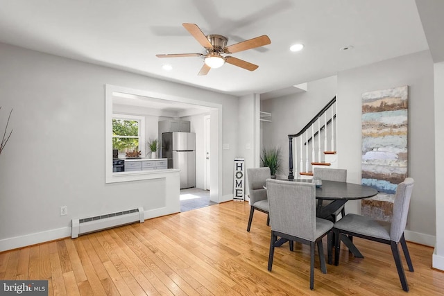 dining area with light wood-type flooring, a ceiling fan, a baseboard heating unit, stairway, and baseboards