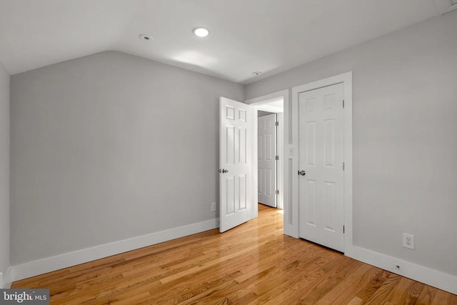 unfurnished bedroom with lofted ceiling, baseboards, and light wood finished floors