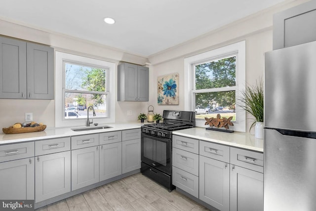 kitchen featuring gray cabinets, freestanding refrigerator, a sink, light countertops, and black range with gas cooktop