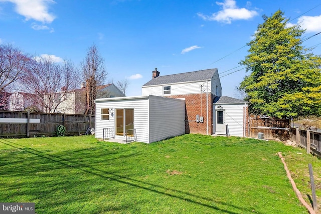 back of house with a lawn, a chimney, a fenced backyard, and brick siding