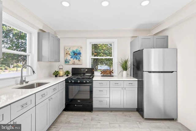 kitchen with gas stove, freestanding refrigerator, gray cabinetry, a sink, and light countertops