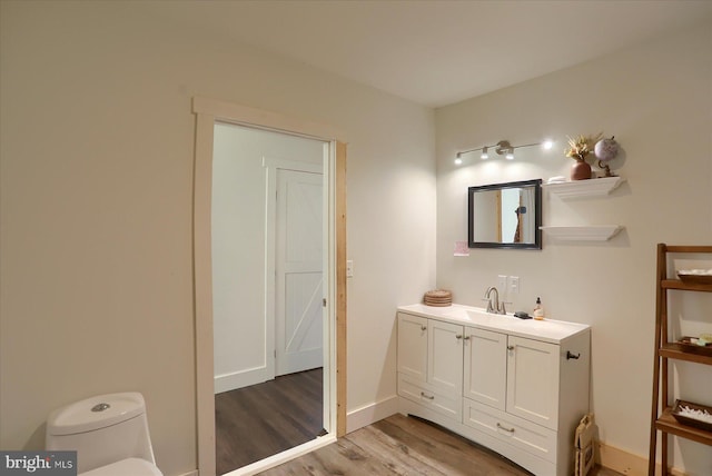 bathroom with vanity, toilet, wood finished floors, and baseboards