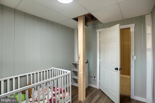 bedroom with a paneled ceiling, a nursery area, and dark wood finished floors