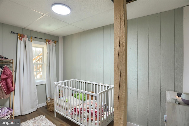 bedroom with a nursery area, wood finished floors, and a drop ceiling