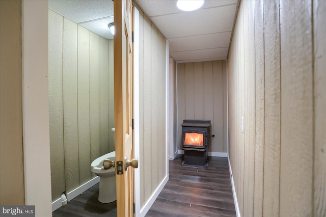 hallway featuring wooden walls, baseboards, dark wood-style flooring, and a drop ceiling