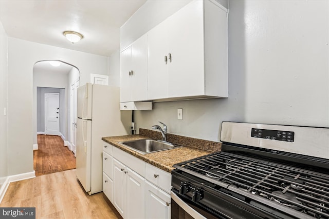 kitchen with light wood-type flooring, a sink, arched walkways, white cabinets, and gas range