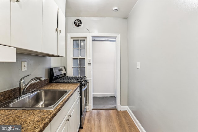 kitchen with visible vents, baseboards, white cabinets, gas stove, and a sink