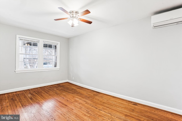 unfurnished room with ceiling fan, an AC wall unit, baseboards, and wood-type flooring