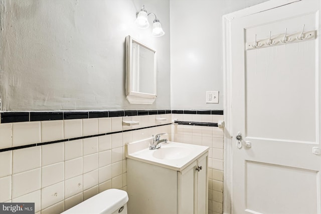 bathroom featuring wainscoting, toilet, vanity, and tile walls