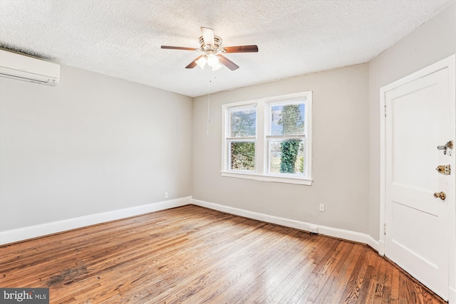 empty room featuring baseboards, a wall unit AC, hardwood / wood-style flooring, a textured ceiling, and a ceiling fan