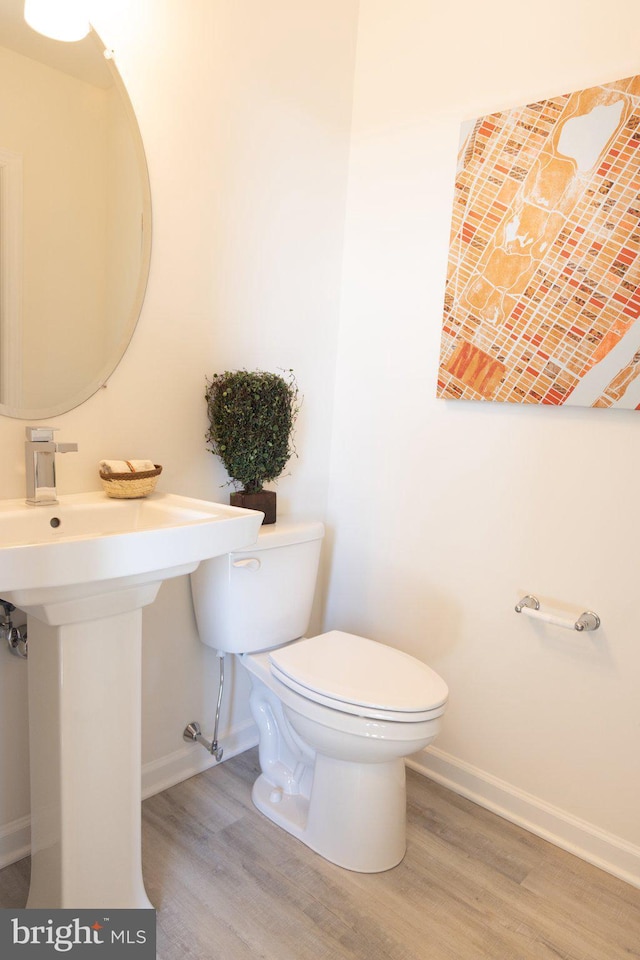 half bath featuring toilet, wood finished floors, baseboards, and a sink