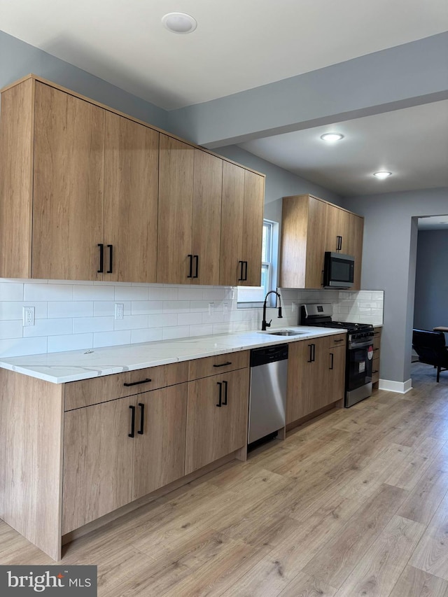 kitchen with light wood-type flooring, a sink, backsplash, stainless steel appliances, and baseboards