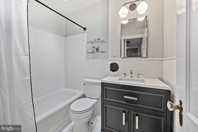 full bath featuring shower / bath combo with shower curtain, toilet, tile walls, vanity, and wainscoting
