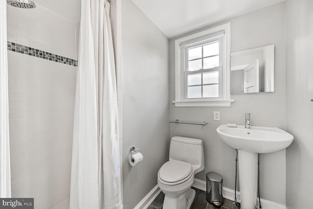 bathroom with toilet, a tile shower, a sink, and baseboards