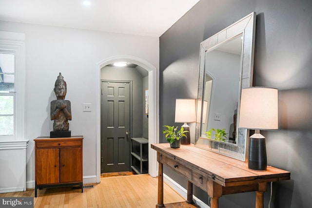 foyer entrance with arched walkways, baseboards, and light wood-type flooring