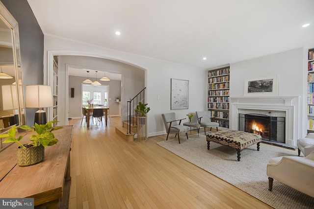 living room featuring stairs, wood-type flooring, baseboards, a lit fireplace, and crown molding