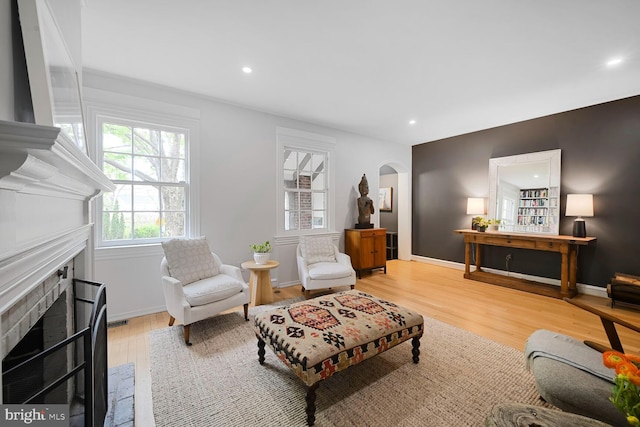 living area featuring recessed lighting, arched walkways, a fireplace with flush hearth, and light wood-type flooring