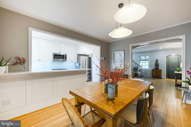 dining space with stairway, arched walkways, and light wood-style flooring