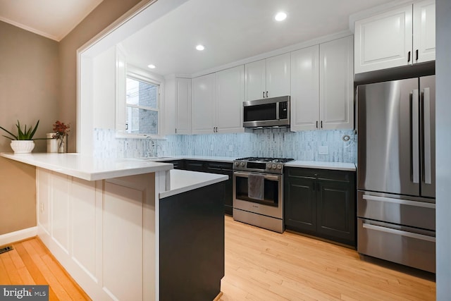 kitchen with tasteful backsplash, stainless steel appliances, light countertops, light wood-type flooring, and a peninsula