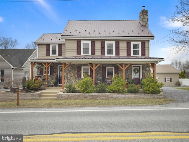 view of front of house featuring stone siding, a porch, a chimney, and metal roof