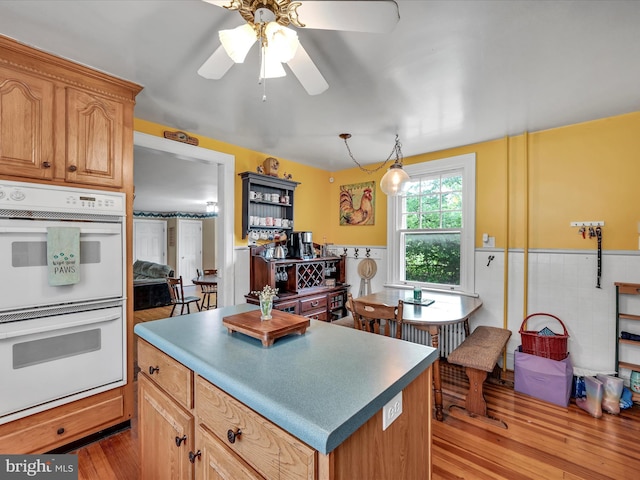 kitchen featuring a wainscoted wall, double oven, a ceiling fan, and light wood finished floors