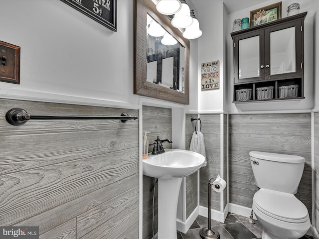 bathroom with tile patterned floors, toilet, a sink, tile walls, and wainscoting