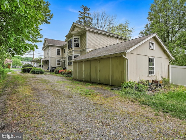 view of side of property with driveway, a shingled roof, and fence