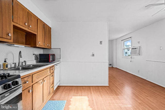 kitchen with dishwasher, light countertops, light wood-type flooring, brown cabinetry, and a sink