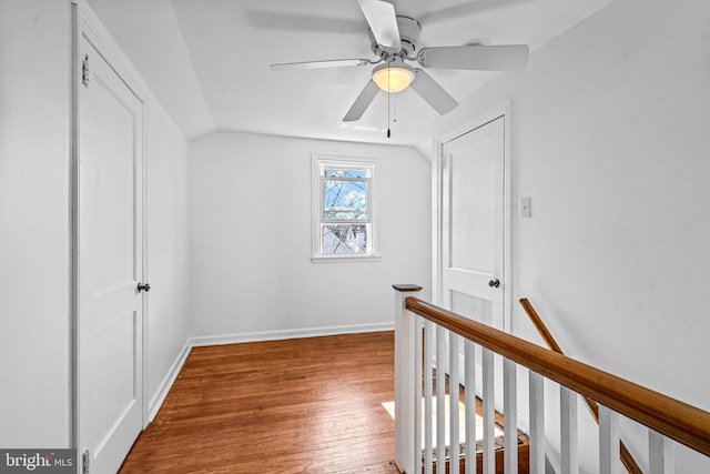 hallway featuring wood finished floors, an upstairs landing, baseboards, and vaulted ceiling