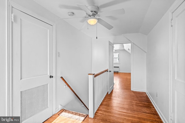 hall featuring wood finished floors, baseboards, lofted ceiling, radiator heating unit, and an upstairs landing