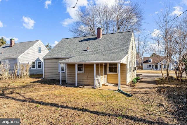 back of house featuring a lawn, roof with shingles, and a chimney