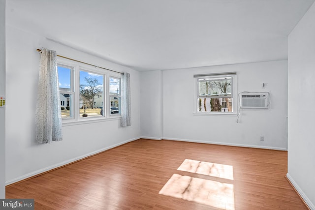 spare room featuring a wall unit AC, baseboards, and wood finished floors