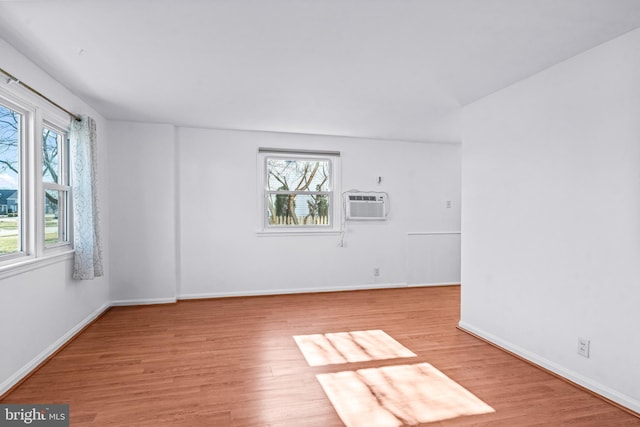 unfurnished room featuring a healthy amount of sunlight, baseboards, light wood finished floors, and a wall mounted AC