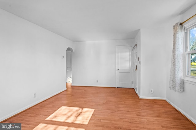 empty room featuring light wood-style floors, arched walkways, and baseboards