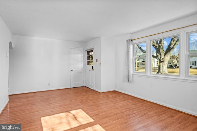 unfurnished room with baseboards, arched walkways, and light wood finished floors