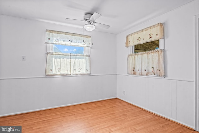 empty room featuring a ceiling fan, wood finished floors, and wainscoting