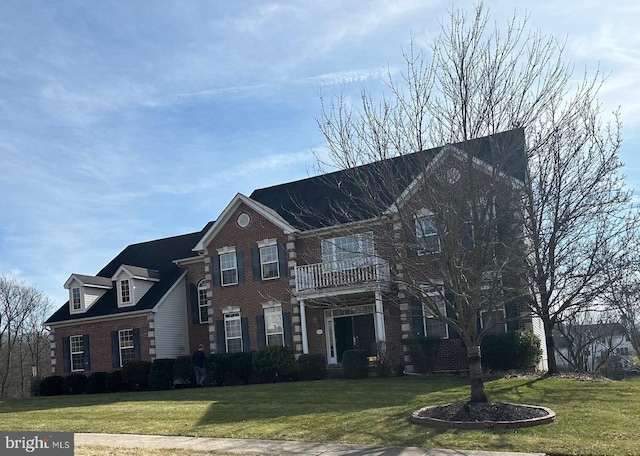 colonial house with brick siding, a balcony, and a front lawn