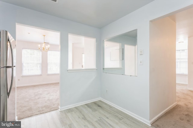 carpeted empty room with baseboards, an inviting chandelier, and wood finished floors