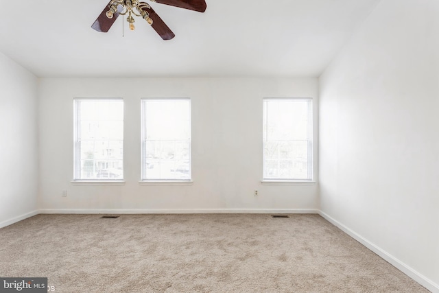 carpeted spare room featuring baseboards, plenty of natural light, and a ceiling fan