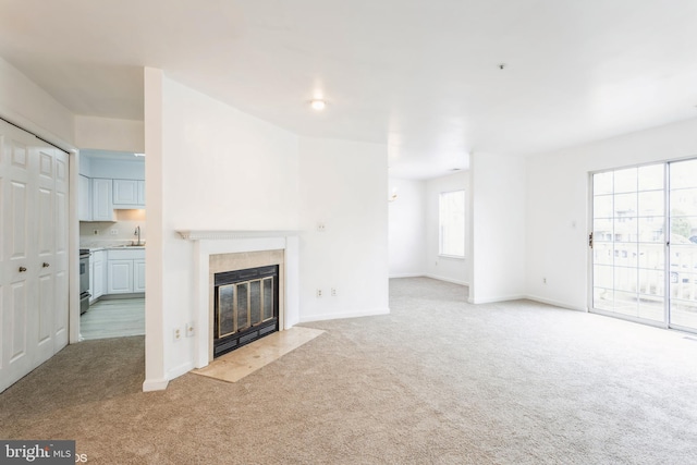 unfurnished living room with a sink, baseboards, carpet floors, and a fireplace with flush hearth