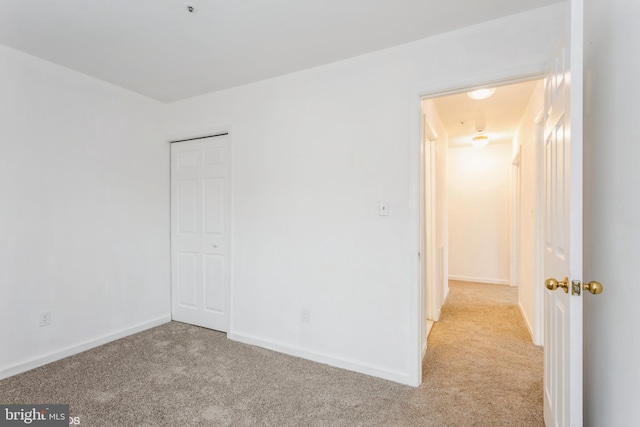 unfurnished bedroom featuring baseboards, a closet, and light carpet