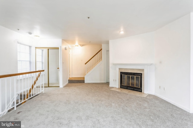 unfurnished living room with a fireplace with flush hearth, baseboards, stairs, and carpet