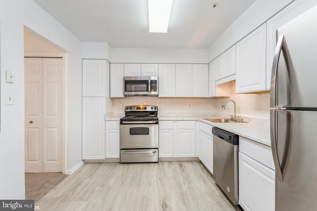 kitchen featuring a sink, appliances with stainless steel finishes, light countertops, and white cabinetry