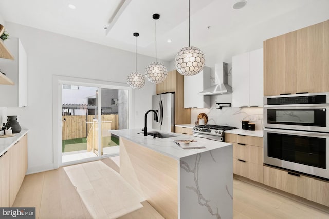 kitchen with wall chimney range hood, modern cabinets, light brown cabinets, and appliances with stainless steel finishes