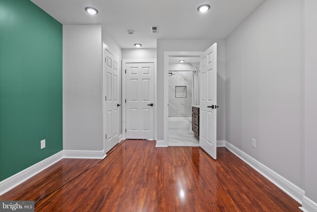 unfurnished bedroom with visible vents, ensuite bath, baseboards, and wood finished floors