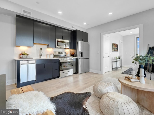 kitchen featuring a sink, dark cabinetry, appliances with stainless steel finishes, light wood finished floors, and light countertops