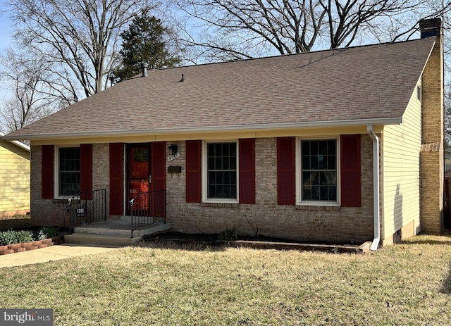 view of front of house with brick siding, a chimney, a front yard, and roof with shingles